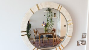 Un espejo redondo con marco de madera que refleja un comedor con una mesa, sillas y una planta colgante.