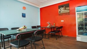 A dining area with a table and chairs, a clock on the wall, and a refrigerator with beverages.