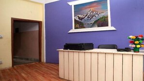 A reception desk with a painting of a mountain landscape, a vase of flowers, and a door leading to another room.