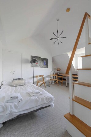 Une chambre moderne avec un lit, un bureau et une chaise. Un escalier mène à un niveau supérieur.