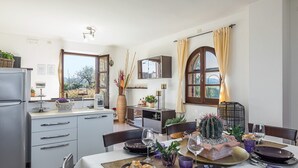 Una cocina moderna con comedor, que incluye un refrigerador, una mesa de comedor para cuatro personas y vistas al exterior a través de amplios ventanales.