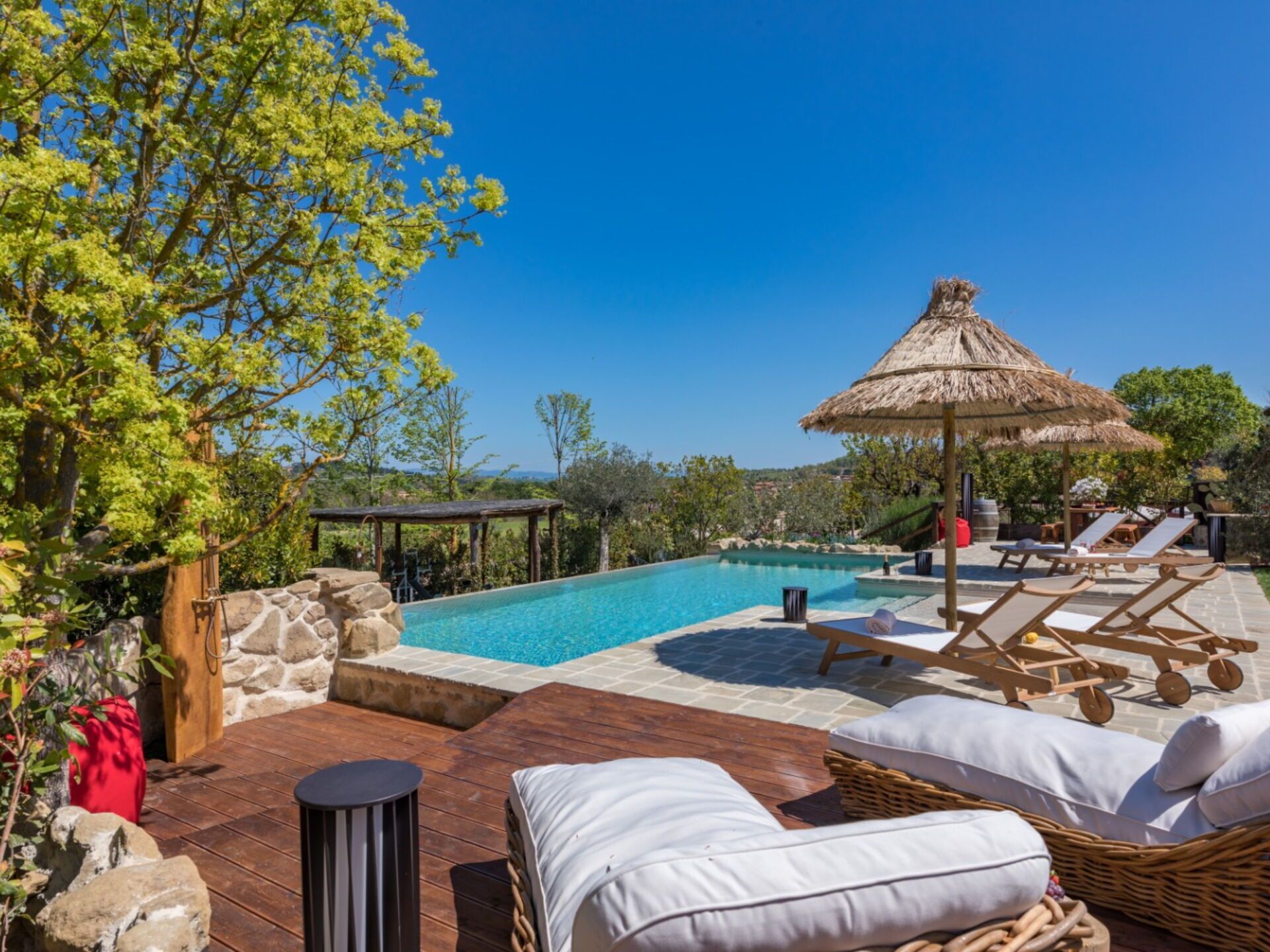 Un espace aménagé au bord de la piscine, avec des chaises longues, un parasol en chaume et un mur en pierre.