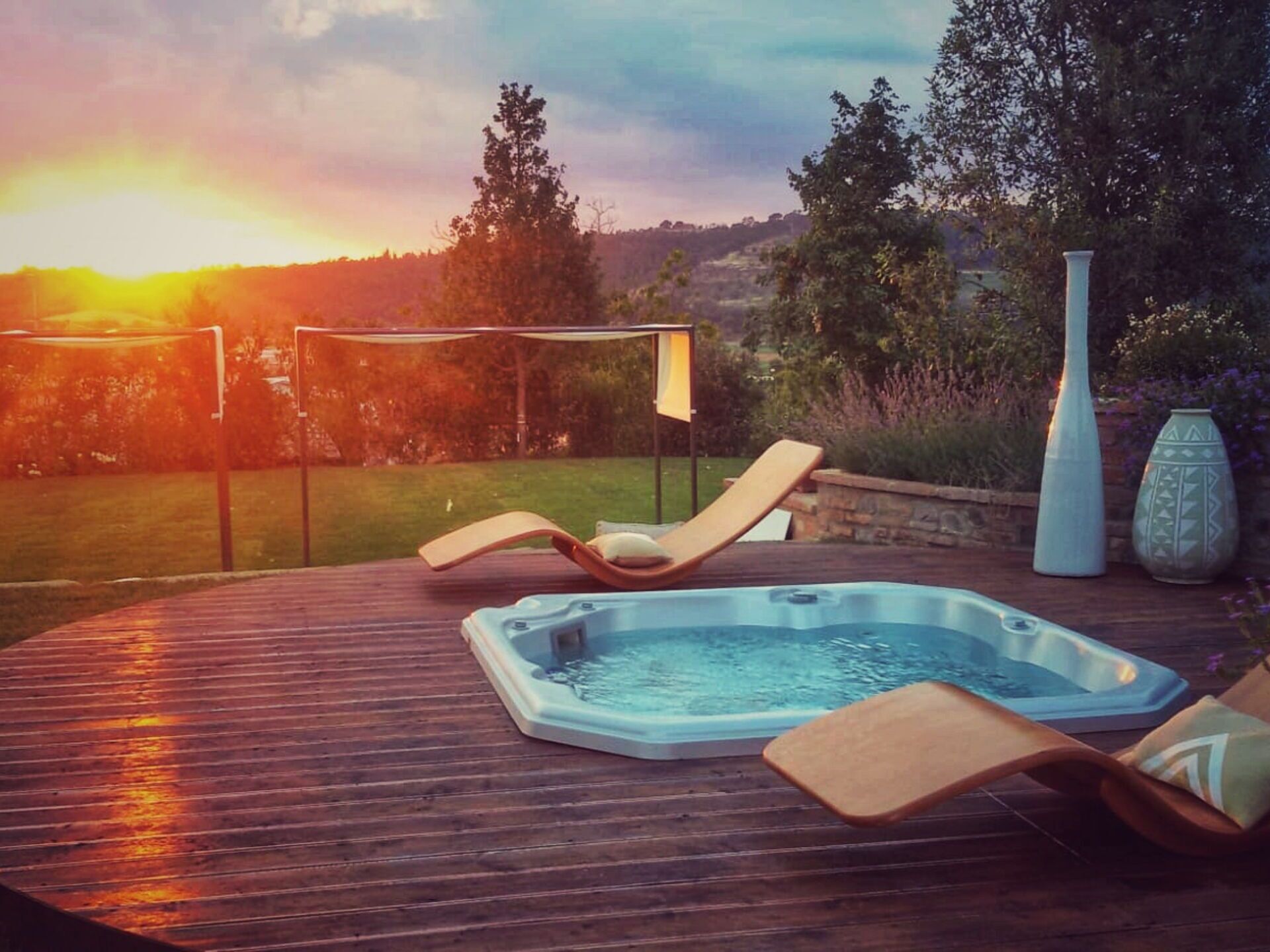 Une terrasse en bois avec un jacuzzi, des chaises longues et un vase blanc.