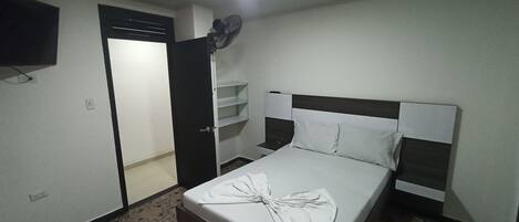 A hotel room with a bed, a TV mounted on the wall, and a door leading to a bathroom.