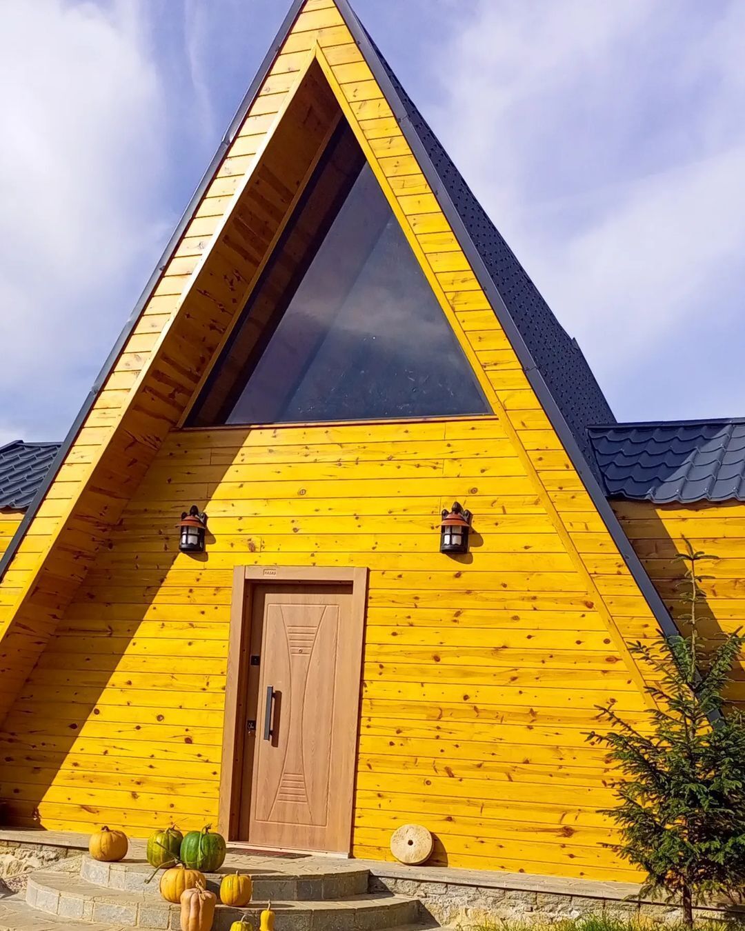 Una construcción de madera triangular con un amplio ventanal triangular y una puerta de madera.