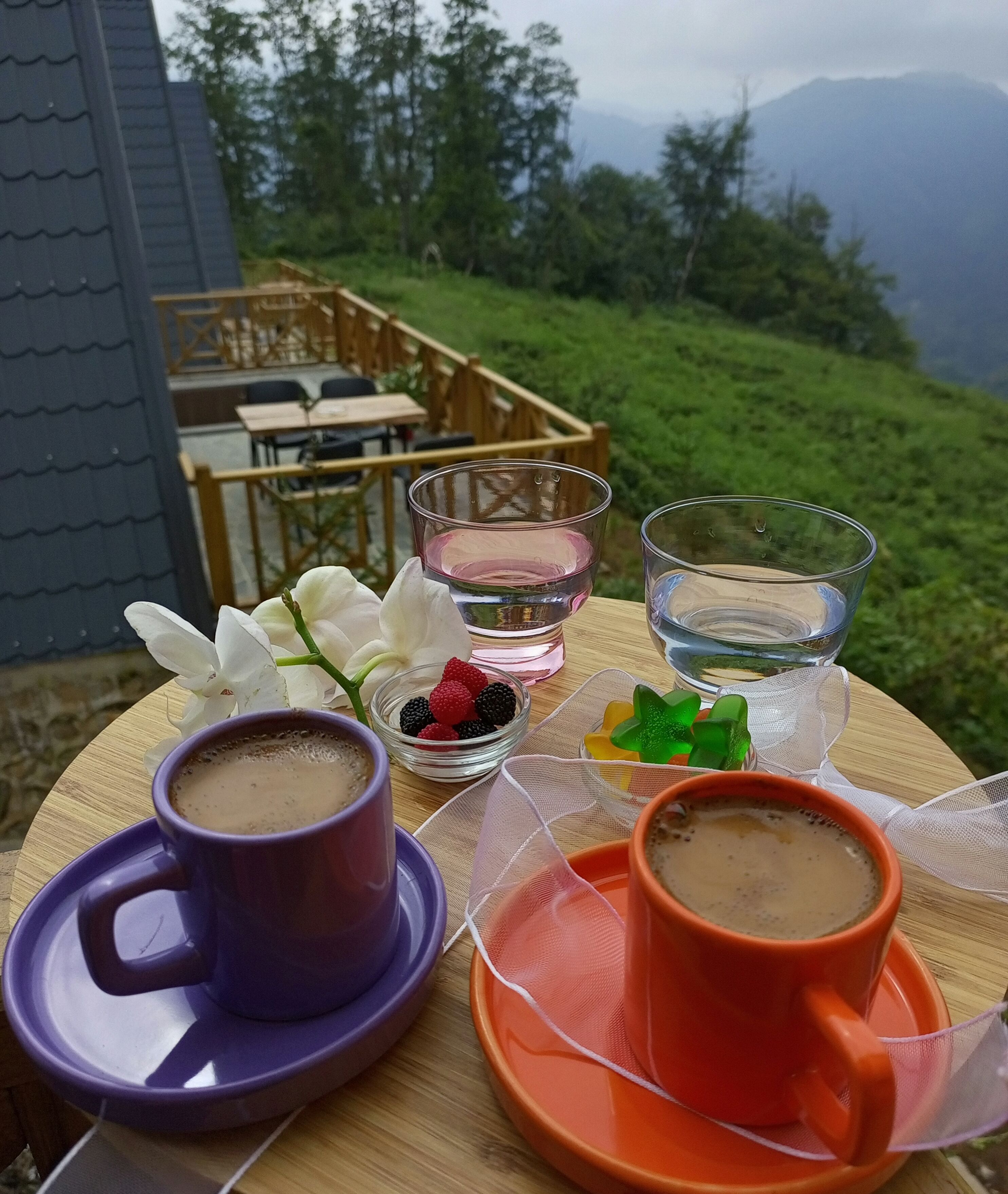 Une table avec deux tasses de café, un verre d’eau et un bol de fruits rouges.