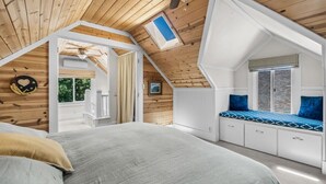 Een slaapkamer met een schuine plafond, dakraam, bed met hoofdeinde, raam met uitzicht en een ingebouwde bank met kussens.