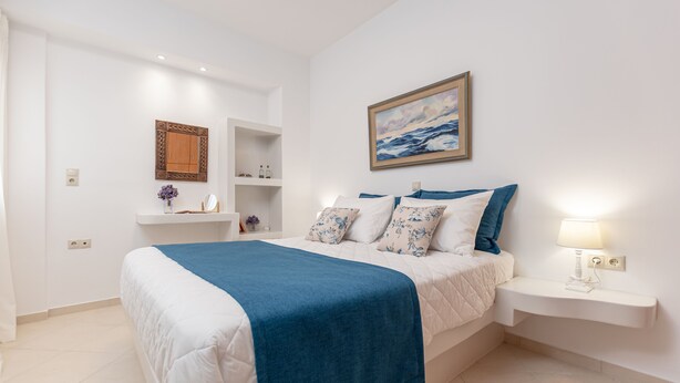 Un dormitorio con cama, mesita de noche, estante en la pared, un cuadro y un armario empotrado.