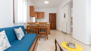 Una sala de estar moderna con un sofá azul, una mesa de comedor de madera y sillas. Se observa un área de cocina al fondo, con armarios de madera y una encimera blanca.