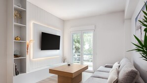 Una sala de estar moderna con un televisor de pantalla plana montado en la pared, una mesa de centro de madera, un sofá gris y un estante blanco con objetos decorativos.