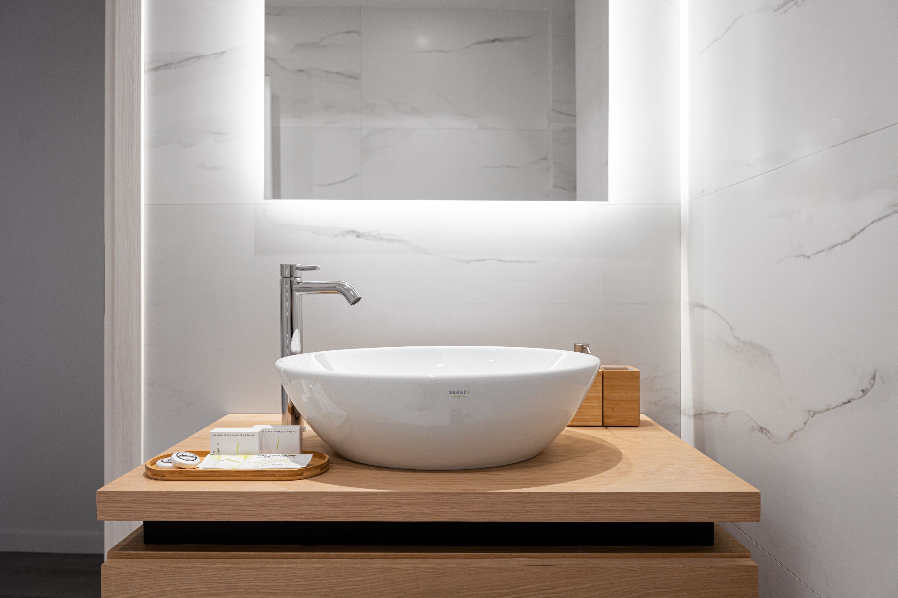 Ein modernes Badezimmer mit einem großen, weißen Waschbecken, einer Holzwaschtischunterschrank und einem Spiegel über dem Waschbecken.