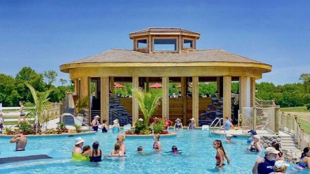 A swimming pool with a gazebo structure, surrounded by greenery and people.