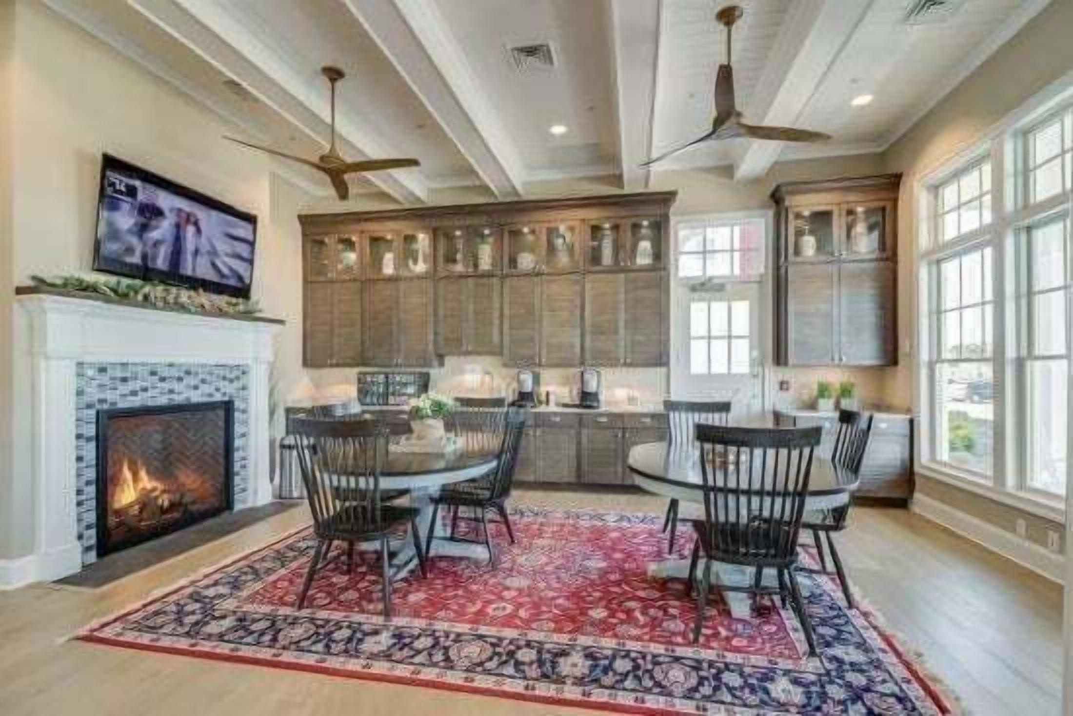 A spacious kitchen with a fireplace, dining area with chairs, and large windows.