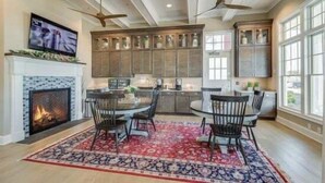 A spacious kitchen with a fireplace, dining area with chairs, and large windows.