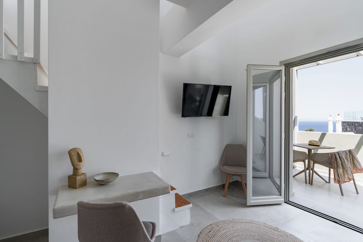 Ein modernes Wohnzimmer im minimalistischen Stil, mit einem an der Wand montierten Flachbildfernseher, einem kleinen Tisch mit einer Schale und einem Sessel.