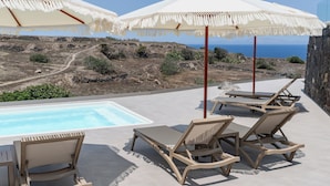 Un espace aménagé au bord de la piscine, avec des chaises longues et des parasols, offrant une vue sur un paysage montagneux et la mer.