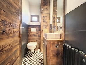 A bathroom with a wooden wall design, a white toilet, a sink with a mirror, and a black radiator.
