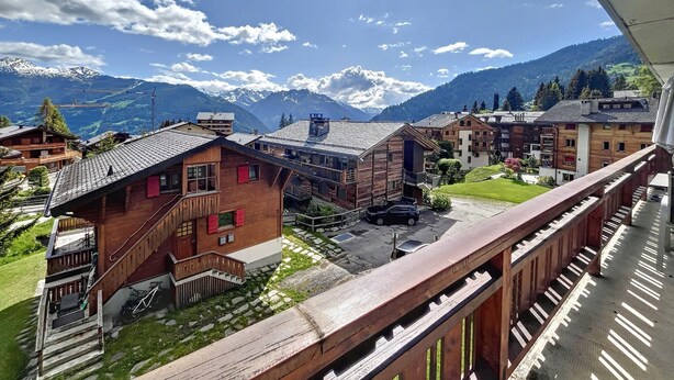 A mountain village with wooden buildings, a clear sky, and snow-capped mountains in the background. - Living room with eating area and a fireplace, a kitchen with dishwasher and Nespresso Coffeemachine, (Verbier)