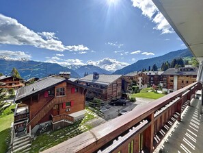 Un village de montagne aux maisons en bois, sous un ciel dégagé, avec des montagnes enneigées en toile de fond.