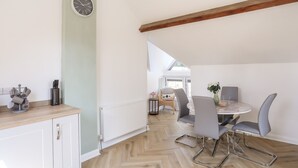 Een eethoek met een ronde tafel, grijze stoelen en uitzicht op het omliggende landschap door een groot raam.