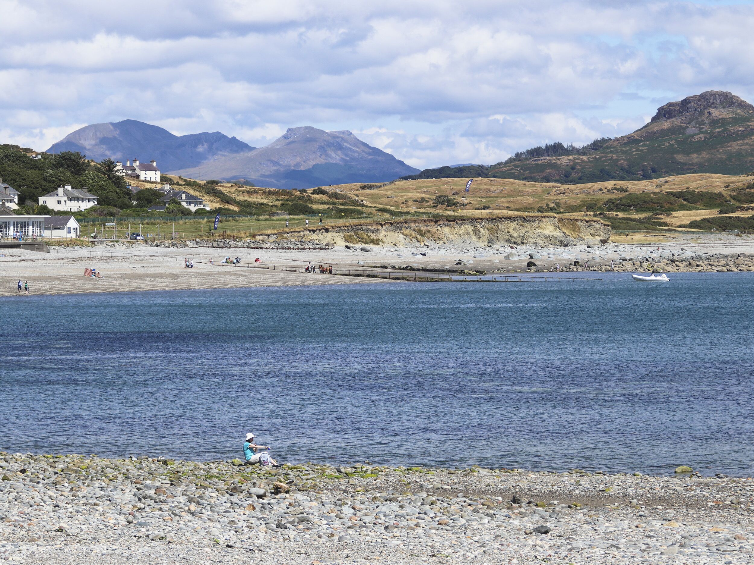 A coastal area with a rocky beach, a small boat, and a person fishing.