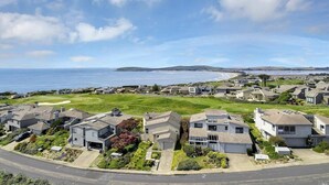 Ett bostadsområde vid kusten med hus, en gräsyta och utsikt över havet.