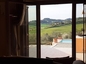A room with a large sliding glass door leading to a pool area with a view of rolling hills and a distant village. - Your nest in the Tuscany countryside (Certaldo - Firenze)