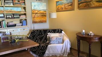 A cozy living room with a patterned sofa, a wooden coffee table, a bookshelf, and two paintings on the wall.