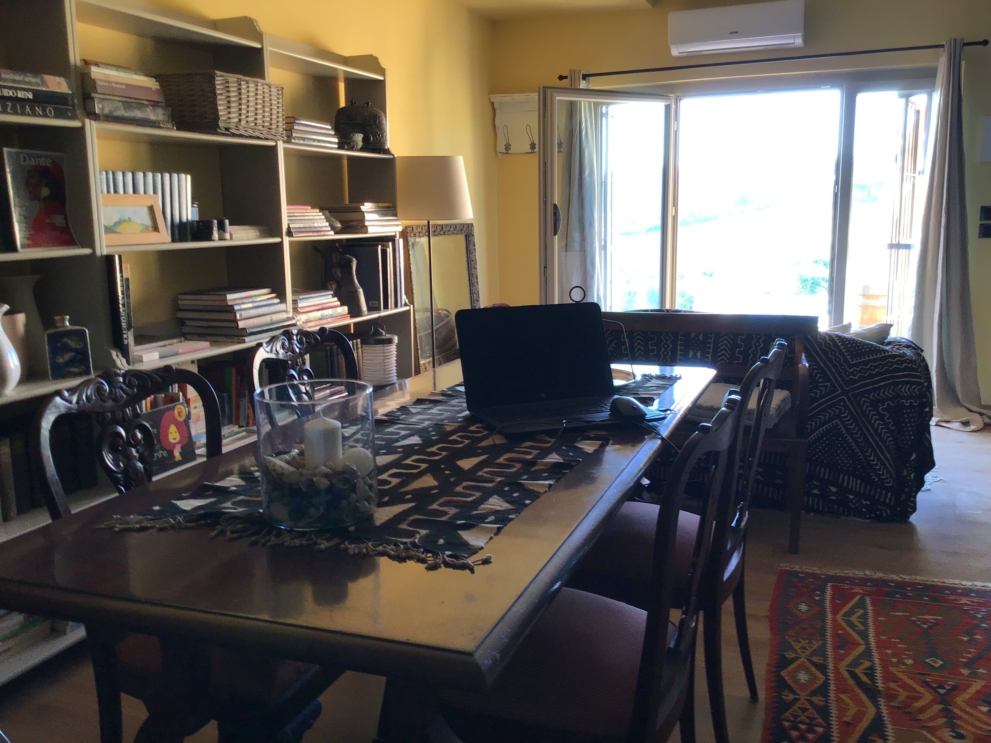 Un salon comprenant une table à manger, des chaises, un ordinateur portable et une bibliothèque remplie de livres et d’objets décoratifs.
