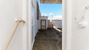 Un estrecho pasillo con paredes blancas, una cuerda a la izquierda y un taburete de madera en el centro.