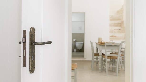 Una puerta blanca con manija metálica y cerradura, que da a una habitación con una mesa de comedor y sillas.