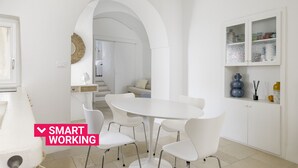Eine moderne Küche mit einem weißen Esstisch und Stühlen, einem weißen Schrank mit Dekorationsobjekten und einem rundbogigen Durchgang zu einem anderen Raum.