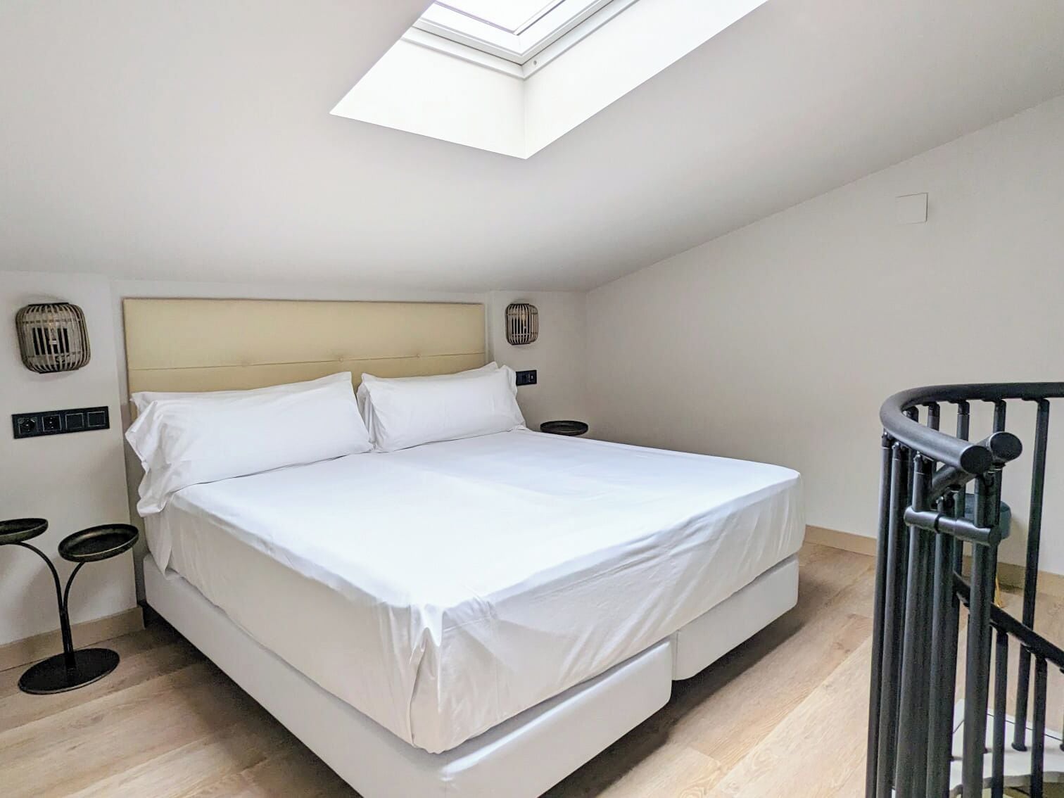 A bedroom with a bed, a skylight, a bedside table, and a chair.