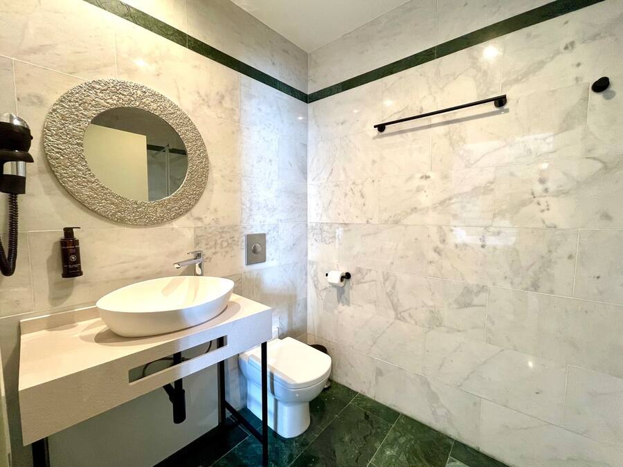 A modern bathroom with a white sink, a round mirror, a toilet, and a towel rack.