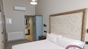 Una habitación de hotel con una cama grande, un cabecero de madera, una mesita de noche y una silla. Se ve un baño al fondo.