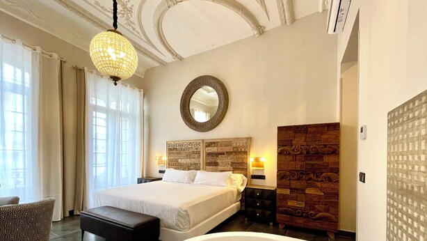 A spacious bedroom with a large bed, a sitting area, a bathtub, and a decorative mirror. - Akla Hotel Badajoz (Badajoz)
