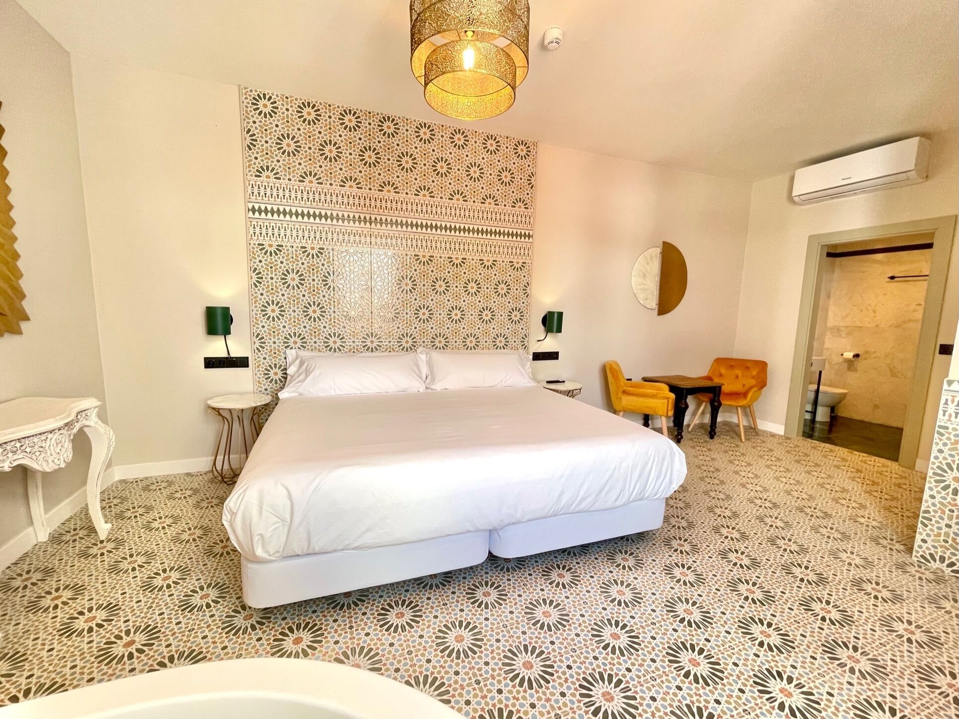 Habitación de hotel con una cama grande, una mesita con dos sillas, aire acondicionado instalado en la pared y suelo estampado.