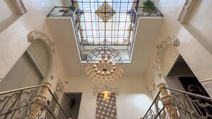 A grand staircase with ornate metal railings and a decorative ceiling light. - Akla Hotel Badajoz (Badajoz)