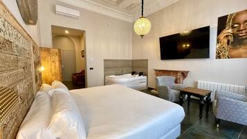 Una habitación de hotel con una cama grande, una zona de estar con una mesa y sillas, un televisor en la pared y un panel decorativo.