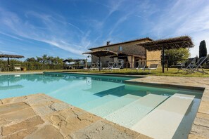 Une piscine avec des chaises longues et, en arrière-plan, un bâtiment en pierre.