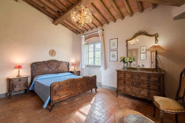 Un dormitorio con cama de madera, cómoda, silla, espejo y candelabro.