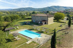 Una vila de pedra amb piscina, envoltada d'un jardí ben cuidat i vistes a turons ondulats.