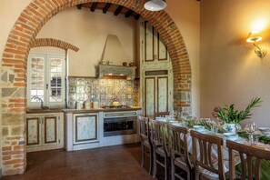 Una cuina amb sostre de rajola arquejat, salabac aules i zona de menjador preparada per a dinar.