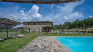 Una piscina de piedra con sillas de descanso, un camino de piedra y un edificio de piedra con un patio.