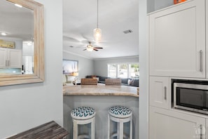 A kitchen with a bar area, a ceiling fan, and a microwave.