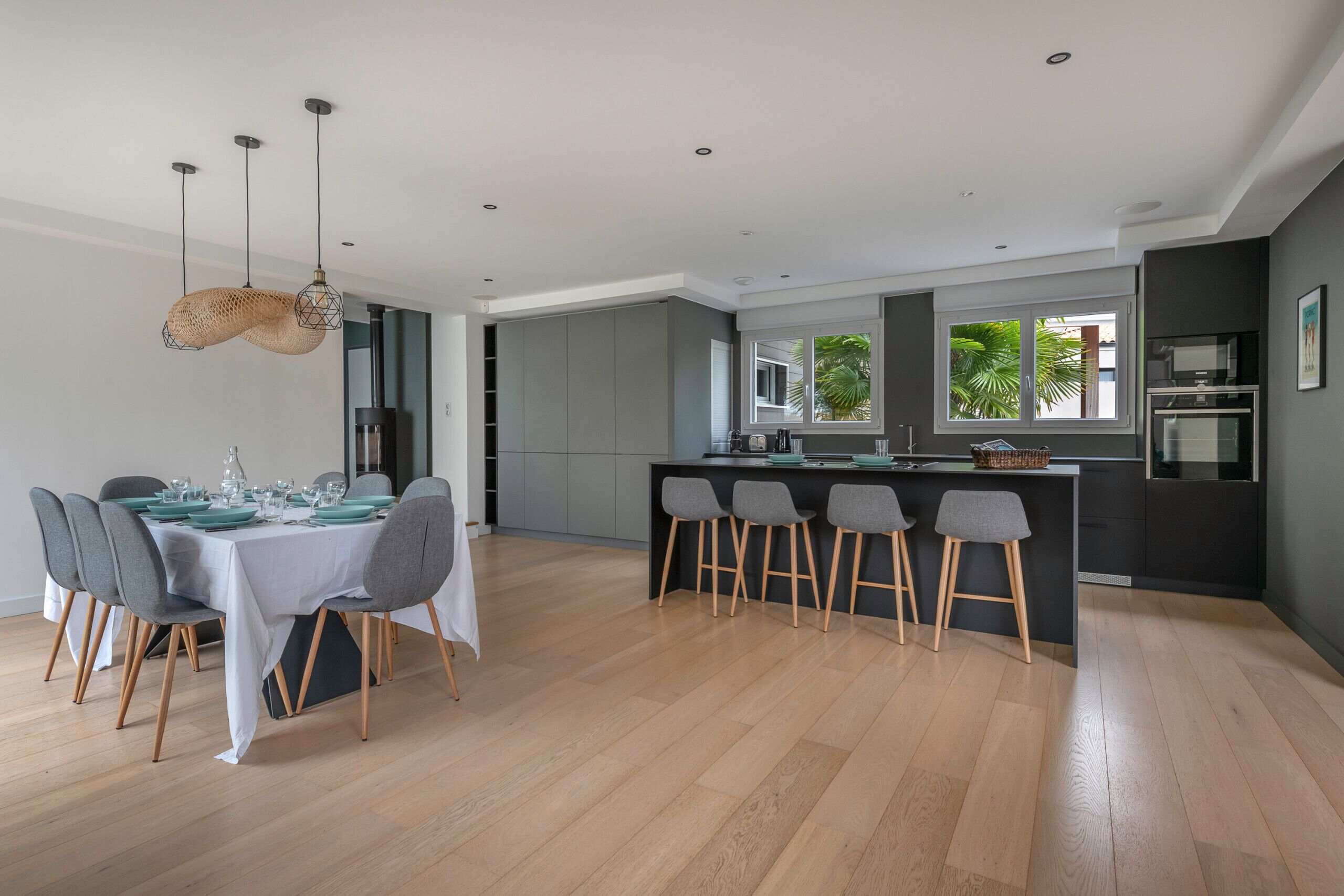 A modern kitchen with grey cabinets, a central island with bar stools, and a dining area with a table set for six.