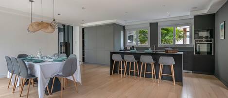 A modern kitchen with grey cabinets, a central island with bar stools, and a dining area with a table set for six.