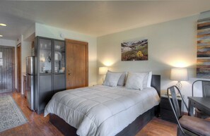 Un dormitorio con cama, armario, escritorio con silla y un cuadro en la pared.