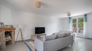 Ein modernes Wohnzimmer mit grauem Sofa, Fernseher, Kamin aus Stein und einem großen Fenster mit Vorhängen.