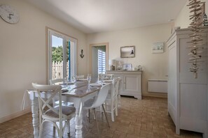 A dining area with a wooden table and white chairs, a white cabinet, and a clock on the wall.